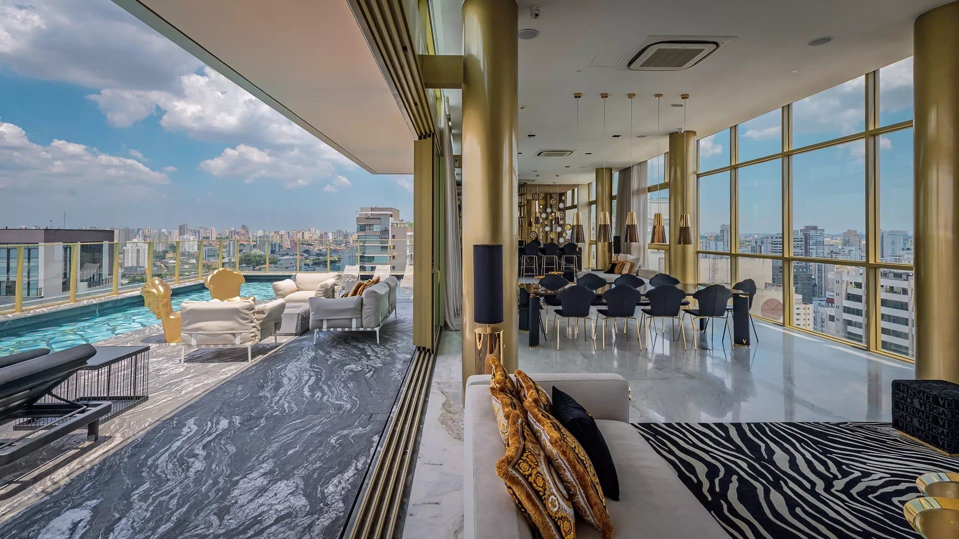 Área de lazer com piscina, espreguiçadeiras, mesas de jantar e vista panorâmica da cidade.