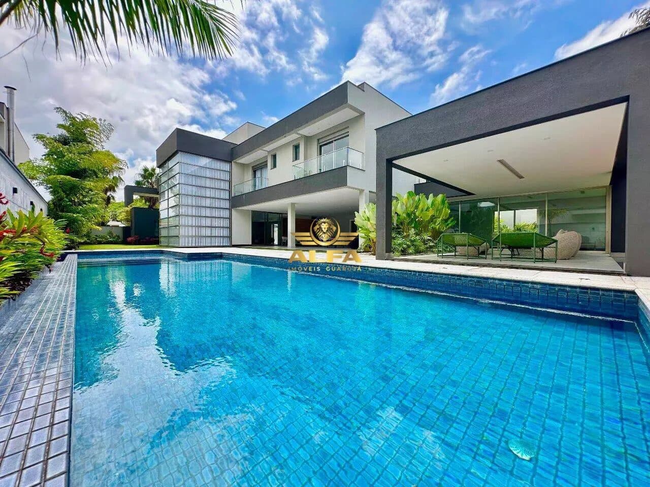 Piscina revestida em tons de azul com área externa e casa ao fundo.